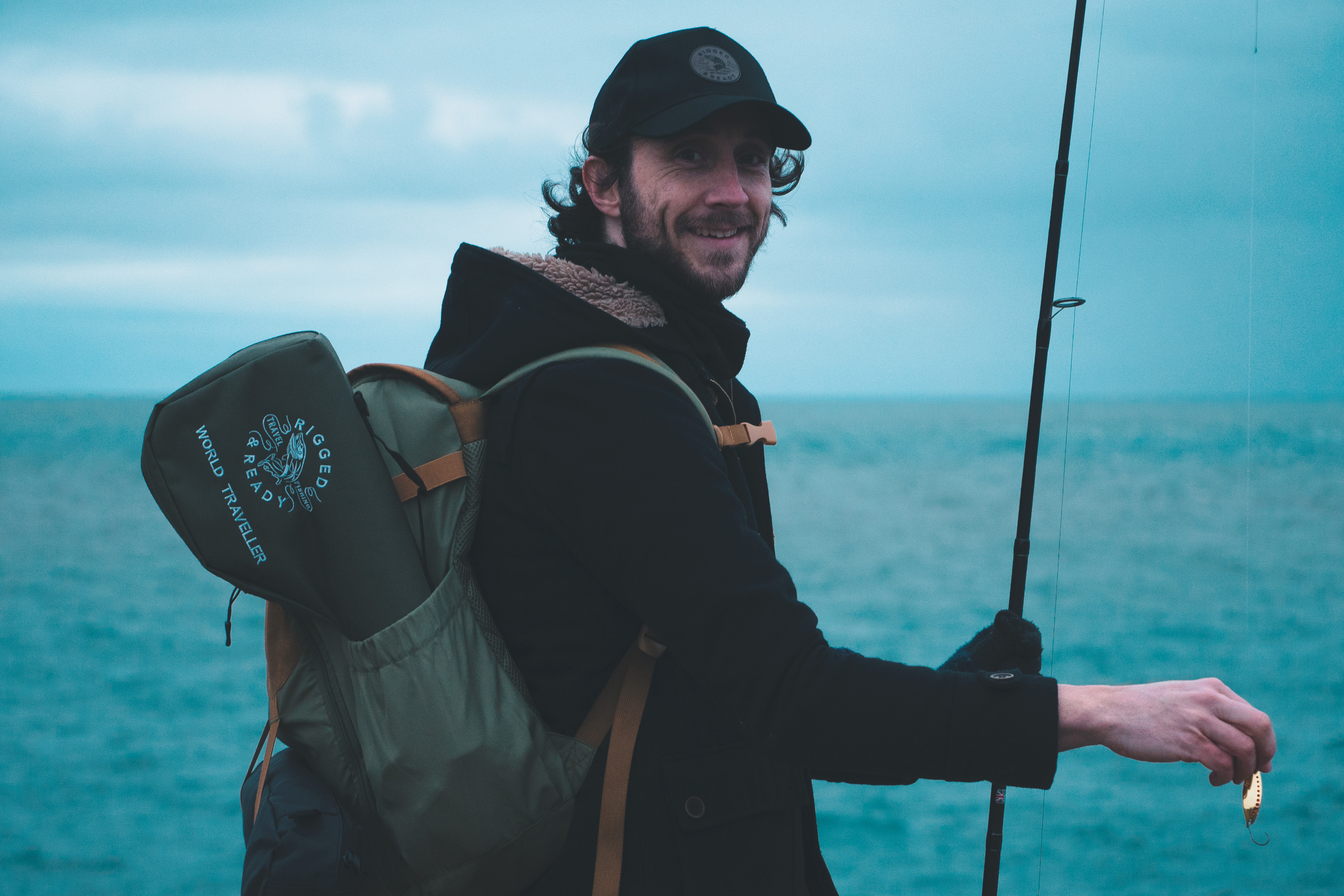 Best Travel Fishing Rods - Photo-real editorial image of a walker seen from behind on a heather moorland pa Smiling angler by the sea holds a rod and lure, with a Rigged and Ready backpack
