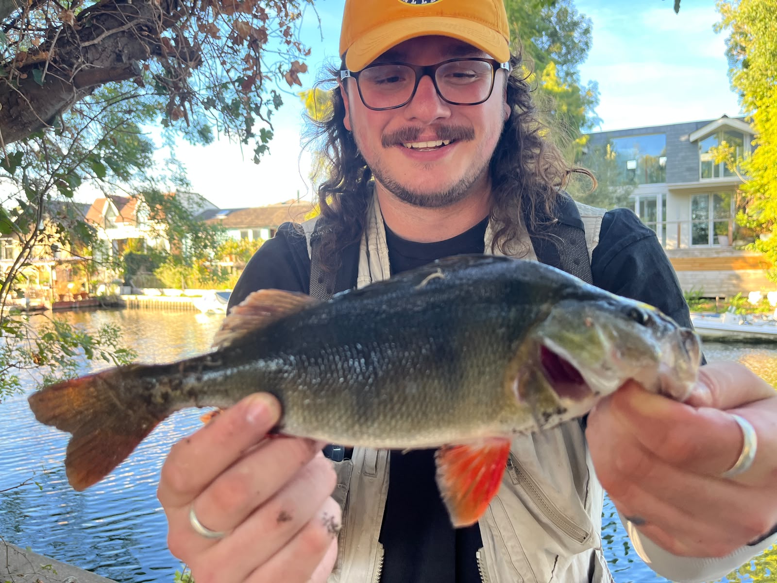 Beginner Fishing Tackle Checklist - Close documentary photograph of an angler's hands, seen from behind and above, t Smiling angler in a yellow cap holds up a perch caught from a riverbank
